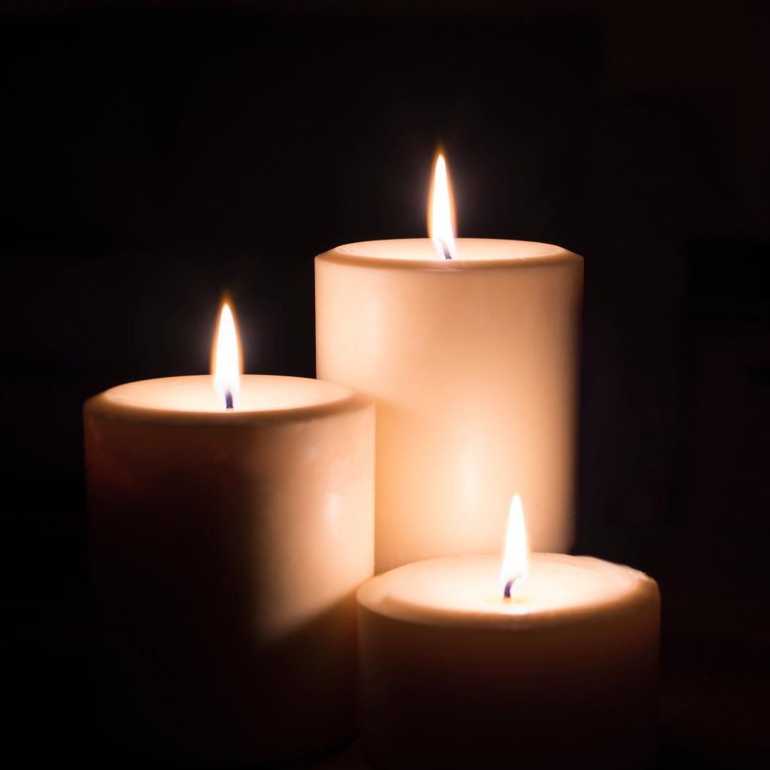 Group of lit ivory beeswax pillar candles on a dark background