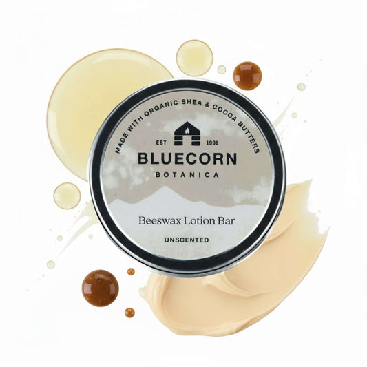 Bluecorn Botanica Beeswax Lotion Bar in Unscented. Made with Organic Shea Butter, Organic Cocoa Butter, Avocado Oil, Apricot Oil, Cappings Beeswax, Essential Oils. Using the warmth of your hands, these solids bars will turn into lotions. Can be used all over the body and come in a convenient tin. Features grey Bluecorn Botanica Label on aluminum tin with opened lid showing lotion bar. Lotion bar is cream in color and features Bluecorn cabin.