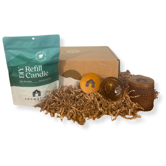 The Woodsy scented DIY candle refill kit with packaging, candle wicks, and a glass container on a white background.