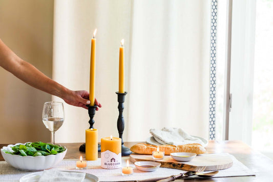 Table setting featuring two beeswax taper candles, salad, bread, and a glass of wine for an elegant dinner.