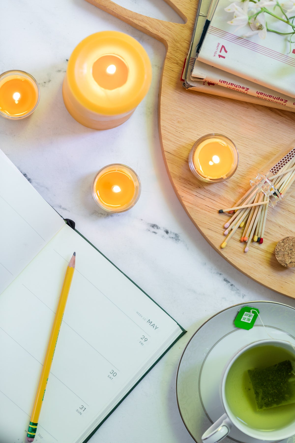 Candlelit scene with a cup of tea, spilled match jar, notebook, and pencil on a table.
