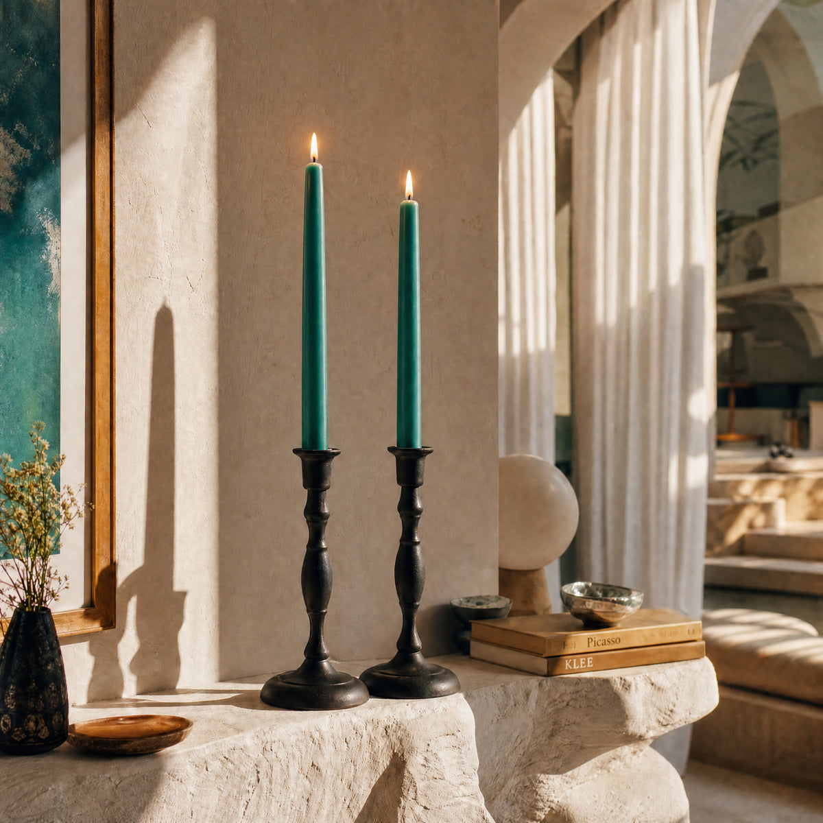 Teal beeswax taper candles in elegant black candlesticks, creating a warm ambiance in a stylish interior.