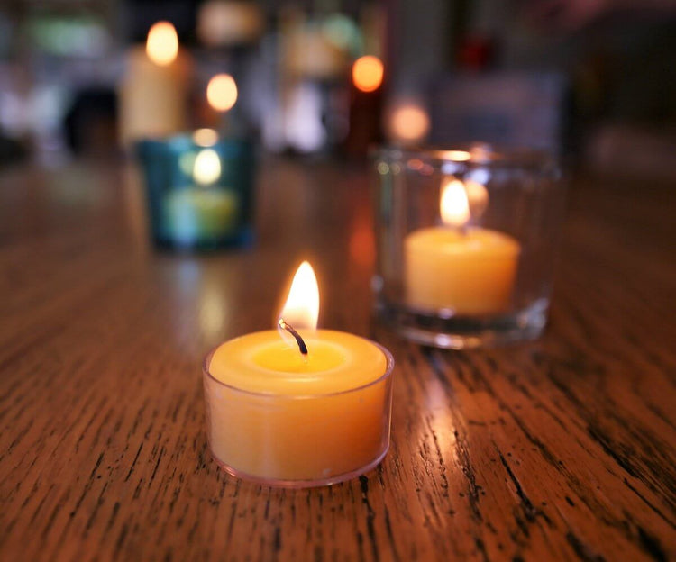 Tea lights glowing softly on a wooden table, showcasing 100% pure beeswax tea light candles in various holders.
