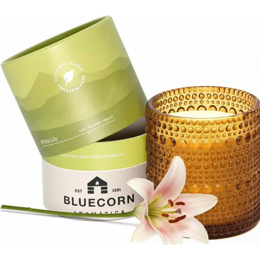 White Lily scented candle from bluecorn aromatica surrounded by lily flowers on a white background