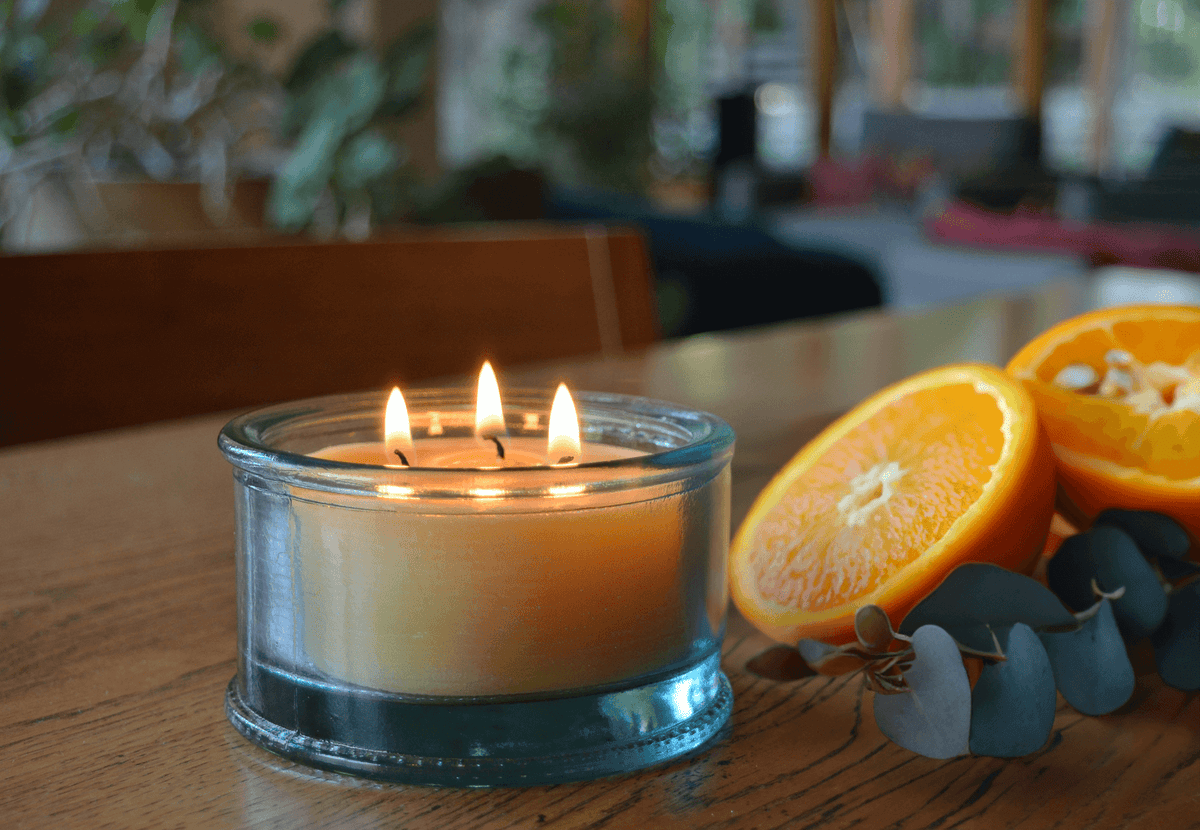 A 3-wick beeswax scented candle in recycled glass, accompanied by sliced oranges on a wooden table.