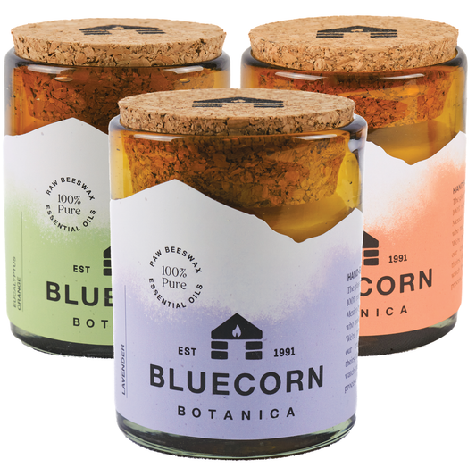 Three filled candles in amber glass jars with Purple, Orange, and Light Green labels - Lavender, Eucalyptus & Orange, Tangerine & Geranium