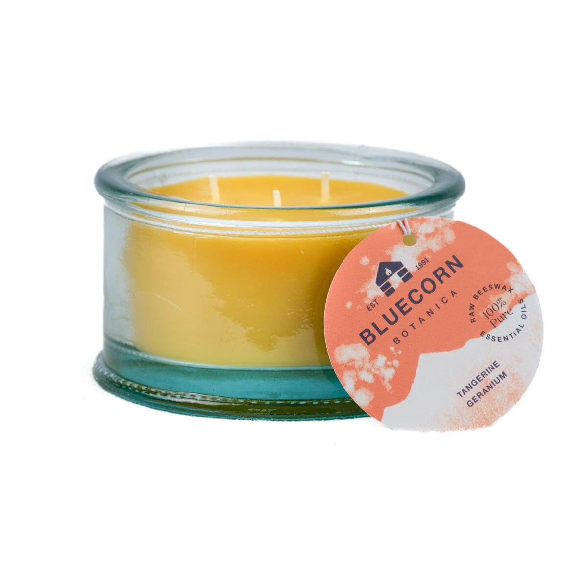 Bluecorn Botanica 100% Pure Beeswax Scented Candle -  Tangerine and Geranium 10oz 3-Wick Glass Candle. Wax is golden in color and glass is clear colored, with a white back drop. Features orange Bluecorn Botanica hang tag printed on 100% recyled paper with Bluecorn name and logo. Burn Time: 18 hours.  Made with 100% Pure Beeswax, 100% Pure Essentail Oils and a 100% pure cotton wick, no lead. Candles are paraffin free, clean burning and non-toxic. 