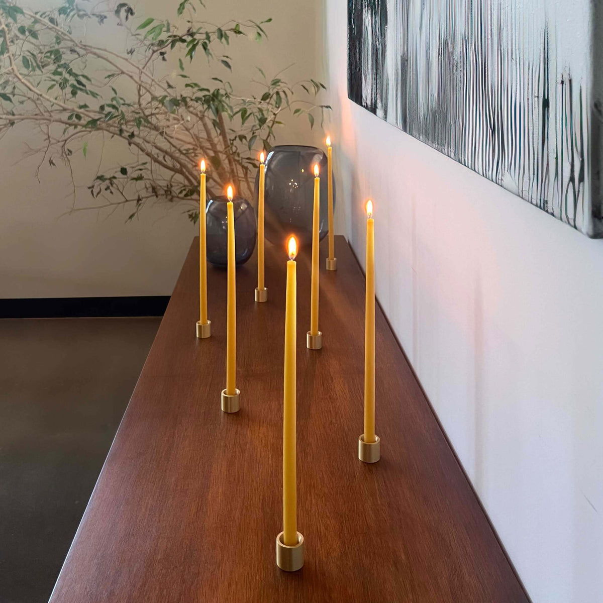 Group of thin beeswax taper candles in solid brass holders on a minimal tabletop