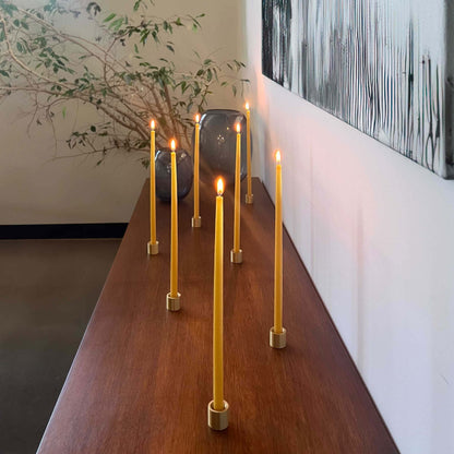 Group of thin beeswax taper candles in solid brass holders on a minimal tabletop