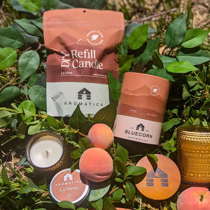 La Mesa scented Bluecorn Aromática Coconut Wax Candles in Sample Tin, Refill Kit, Small & Large glass lying in grass with peaches