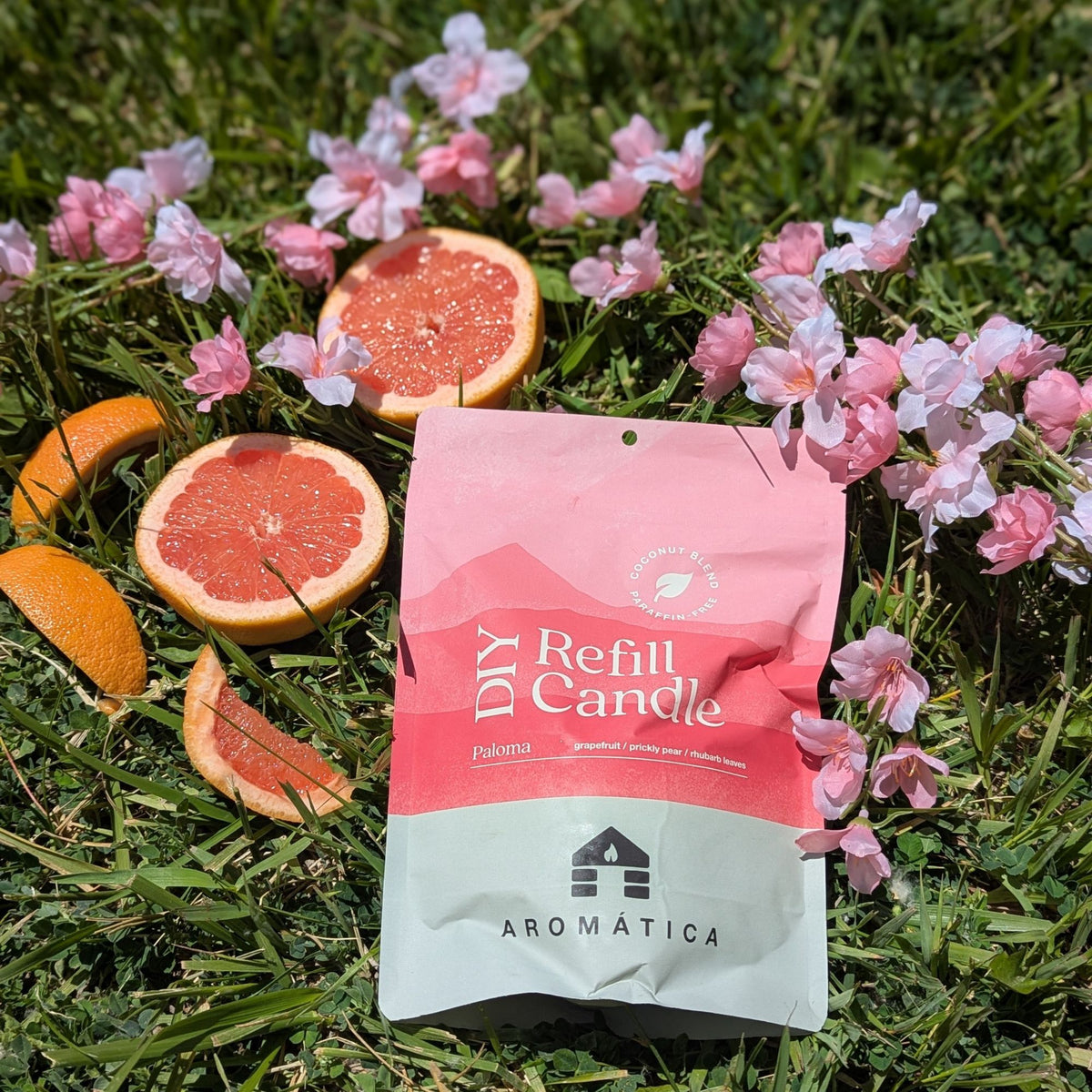Paloma scented Bluecorn Aromática DIY refill kit lying in grass with grapefruit slices and pink flowers