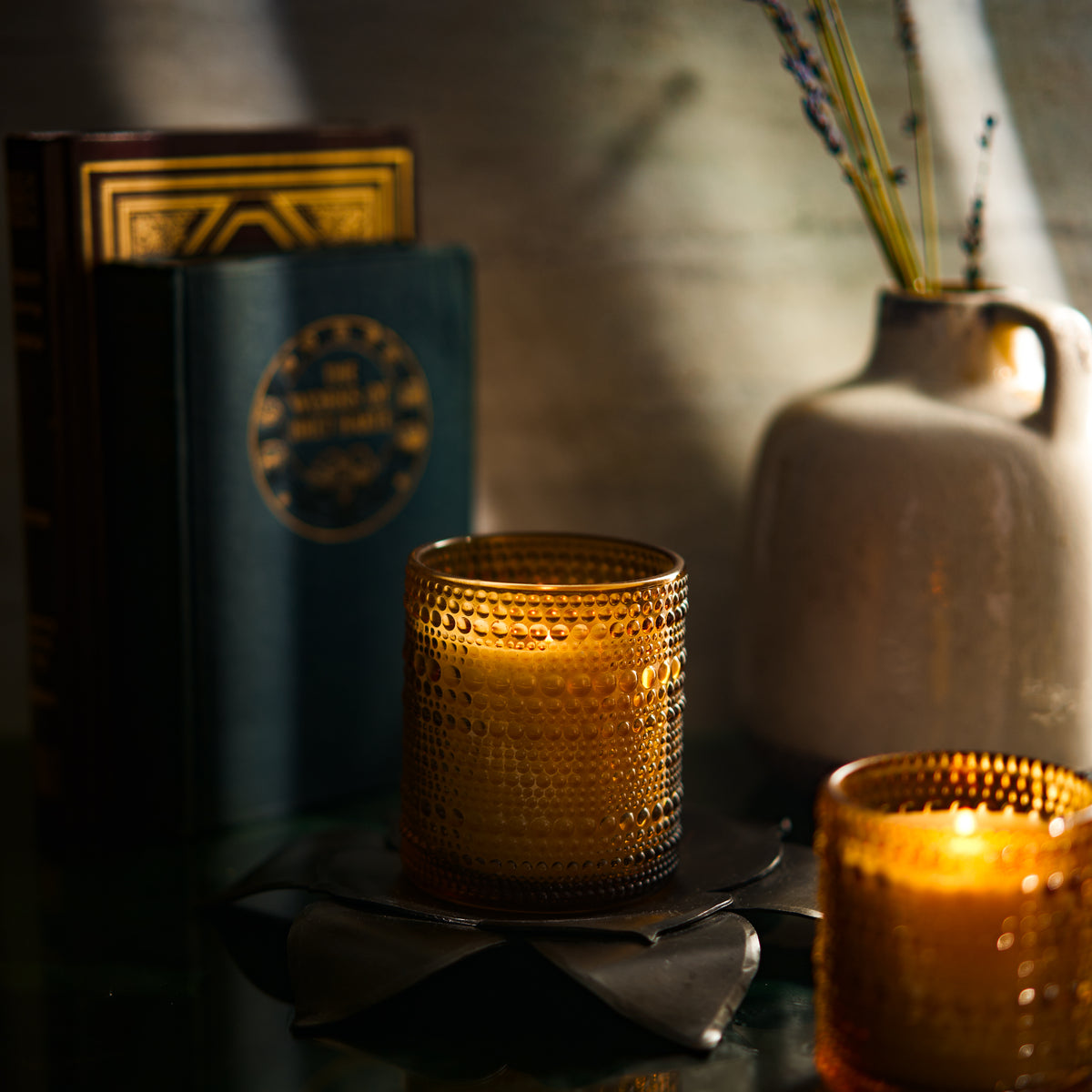 Winter scented candle glowing softly beside a book and vase, creating a cozy ambiance. 