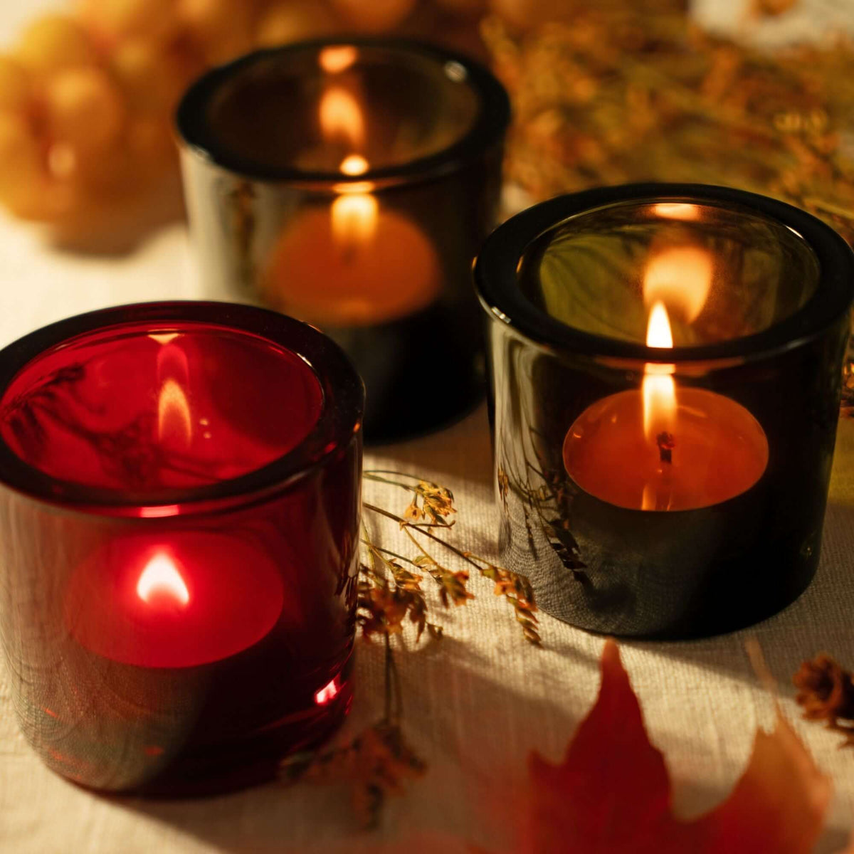 Glowing beeswax tea light candles in heavy glass holders with seasonal greenery