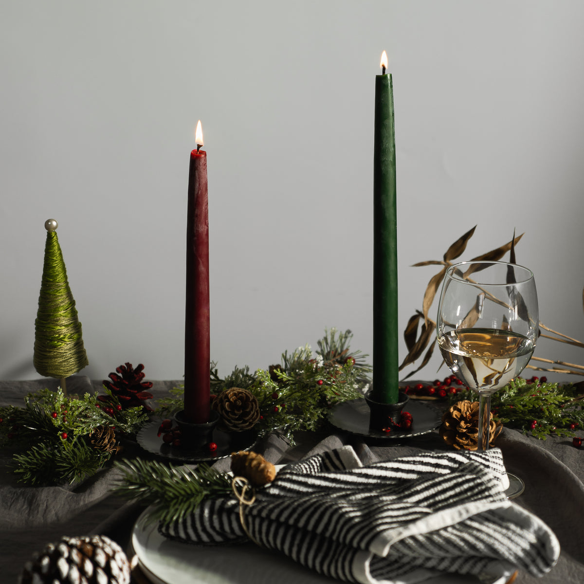 Bluecorn Beeswax hand-dipped burgundy and moss taper candles in  Hand Forged taper holder on Christmas tablescape with folded napkin and glass of white wine. 