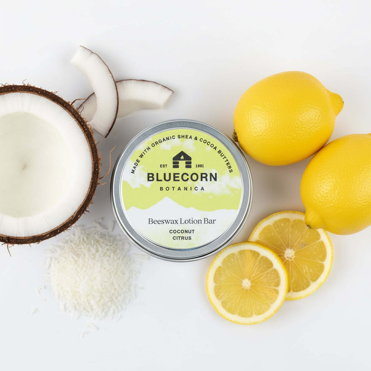 Bluecorn Botanica Beeswax Lotion Bar in Coconut Citrus. Made with Organic Shea Butter, Organic Cocoa Butter, Avocado Oil, Apricot Oil, Cappings Beeswax, Essential Oils. Using the warmth of your hands, these solids bars will turn into lotions. Can be used all over the body and come in a convenient tin. Features green Bluecorn Botanica Label on aluminum tin with opened lid showing lotion bar. Lotion bar is cream in color and features Bluecorn cabin.