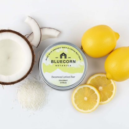 Bluecorn Botanica Beeswax Lotion Bar in Coconut Citrus. Made with Organic Shea Butter, Organic Cocoa Butter, Avocado Oil, Apricot Oil, Cappings Beeswax, Essential Oils. Using the warmth of your hands, these solids bars will turn into lotions. Can be used all over the body and come in a convenient tin. Features green Bluecorn Botanica Label on aluminum tin with opened lid showing lotion bar. Lotion bar is cream in color and features Bluecorn cabin.