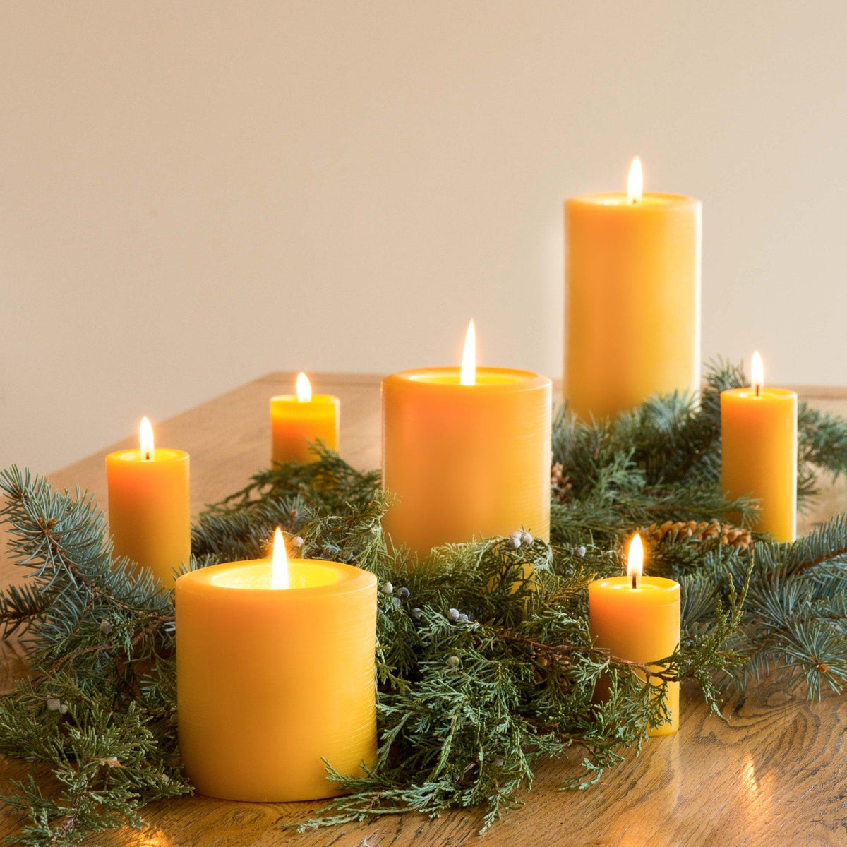 Raw beeswax pillar candles grouped with fresh pine branches