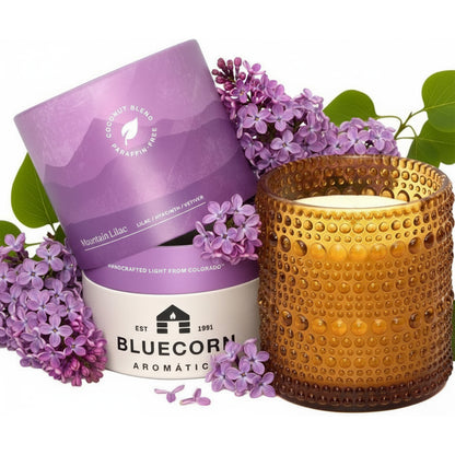 Lilac scented candle from bluecorn aromatica surrounded by Lilac flowers on a white background