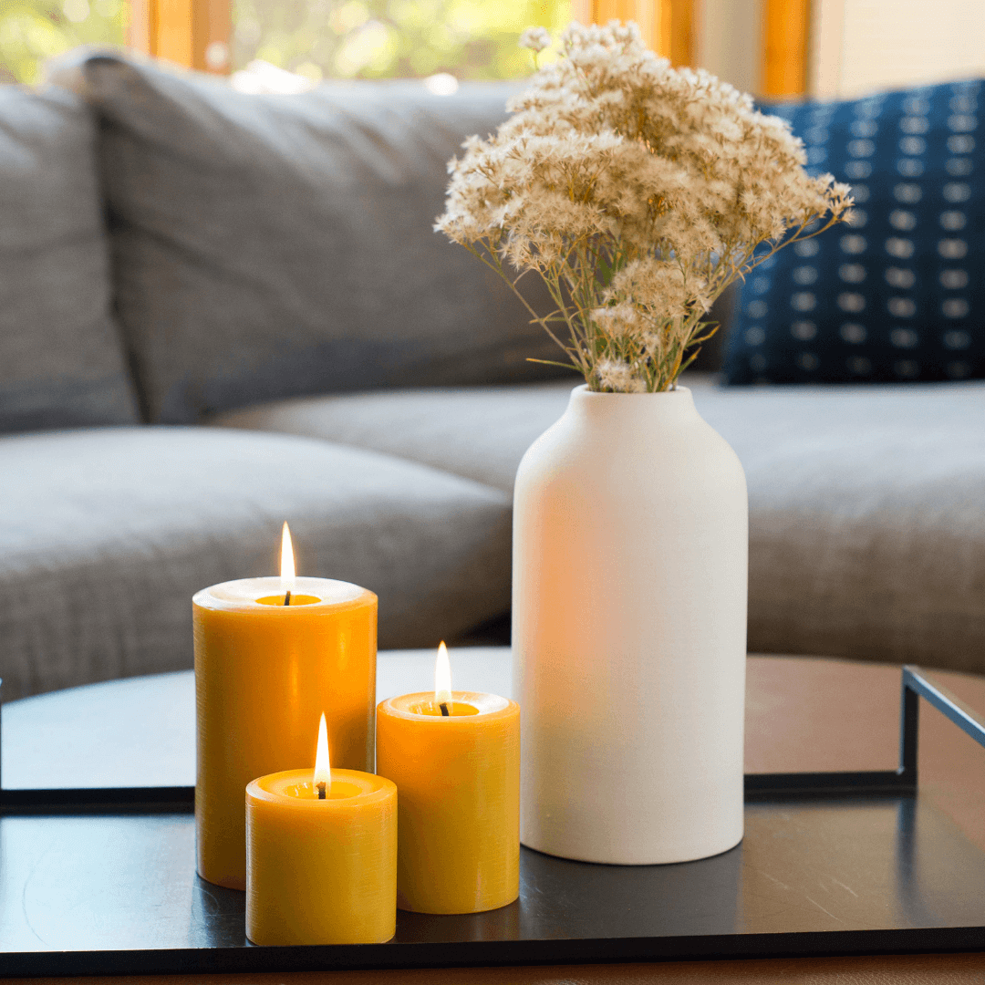 3 Bluecorn Beeswax pillar candles that are lit in a decorative setup with candles and a vase on a coffee table in a living room.
