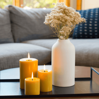 3 Bluecorn Beeswax pillar candles that are lit in a decorative setup with candles and a vase on a coffee table in a living room.
