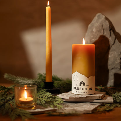 Hand-dipped beeswax taper candles on display with natural decor, emitting warm light and a honey scent.