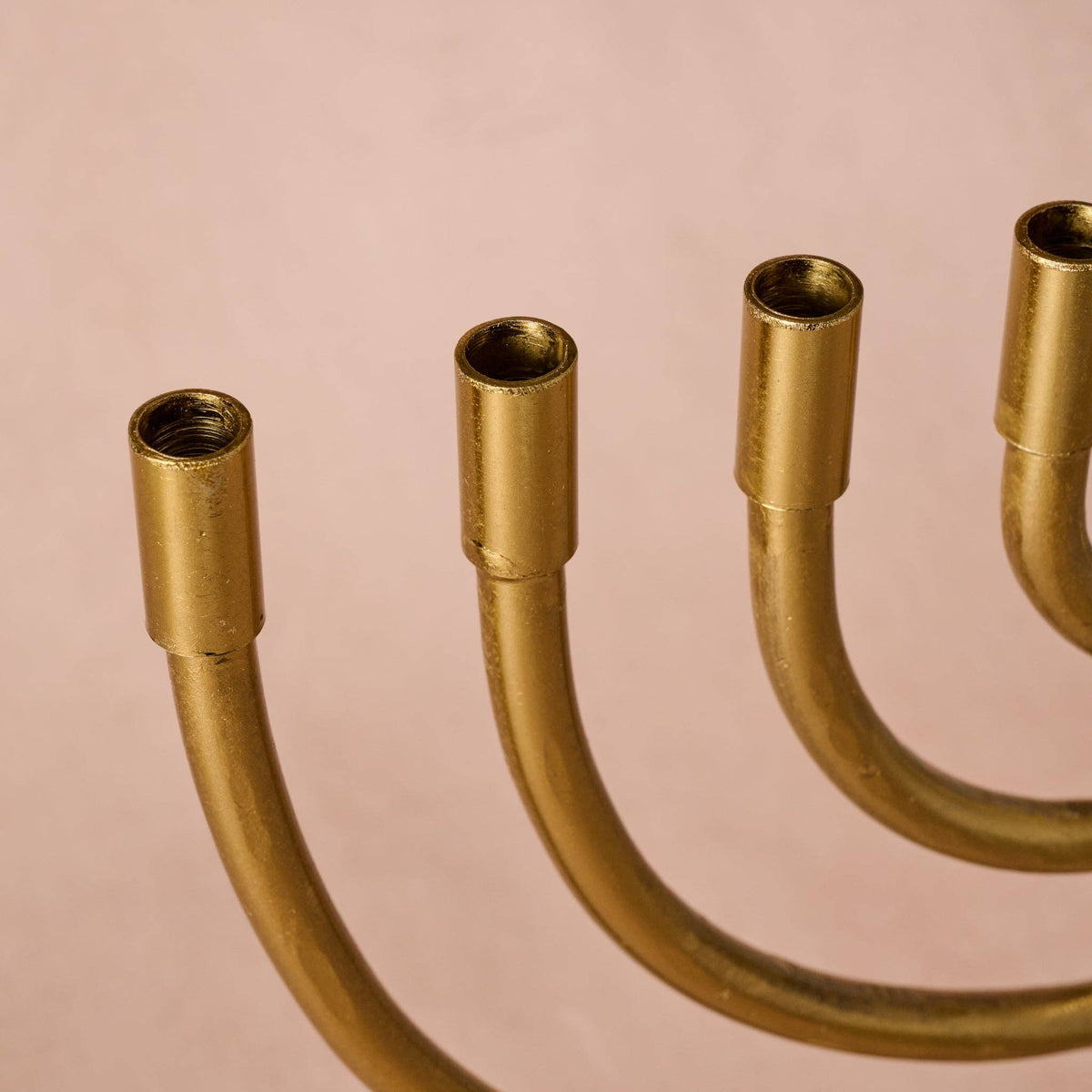 Close-up of a brass candelabra showing the five candle holders and curved arms against a solid pale pink background.