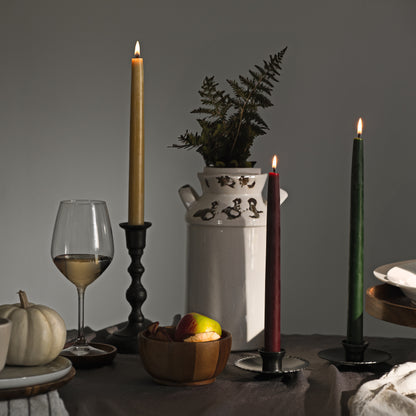 Bluecorn Beeswax hand-dipped burgundy, raw and moss taper candles in  Hand Forged taper holder on thanksgiving tablescape with milk jug filled with greenery and glass of white wine. 