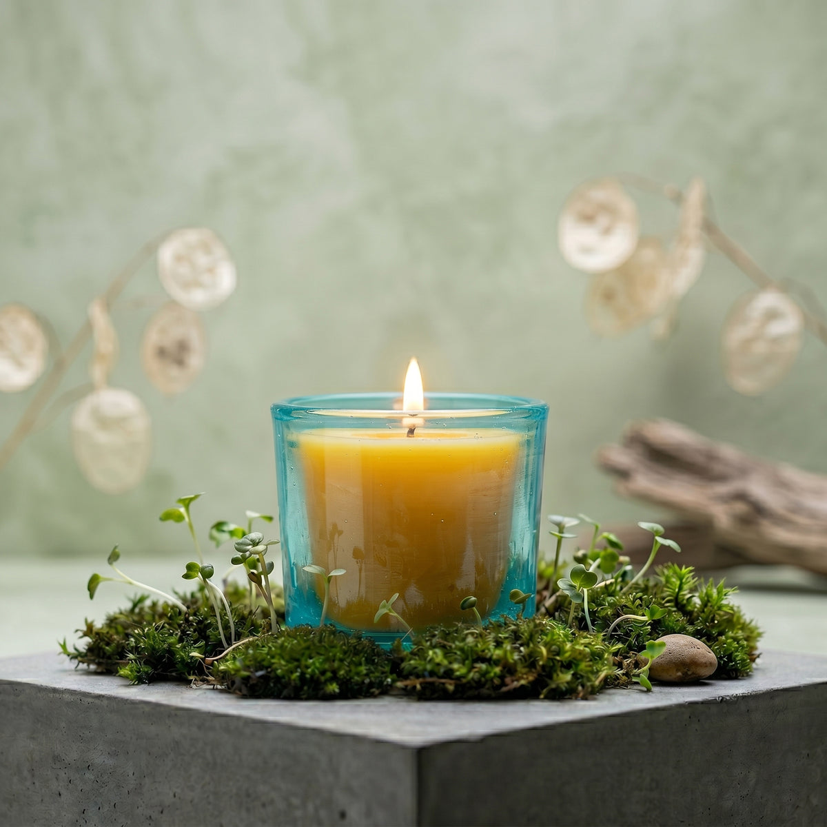 Aqua votive candle holder with beeswax candle, surrounded by moss, showcasing bright and eco-friendly design.