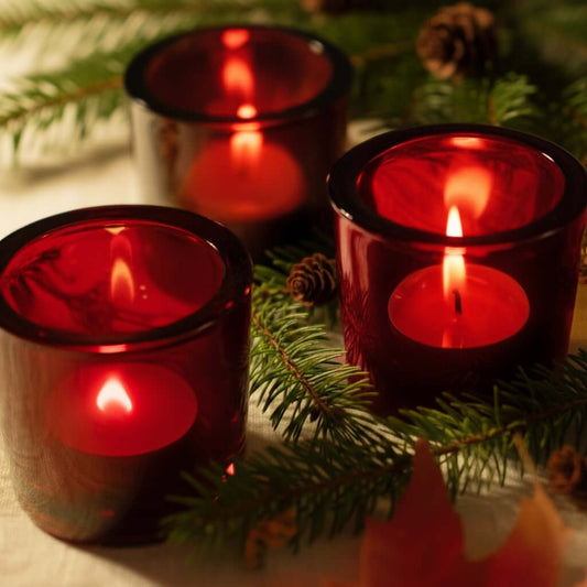 Tea Light candles burning in red glass votive holders with holiday decor background