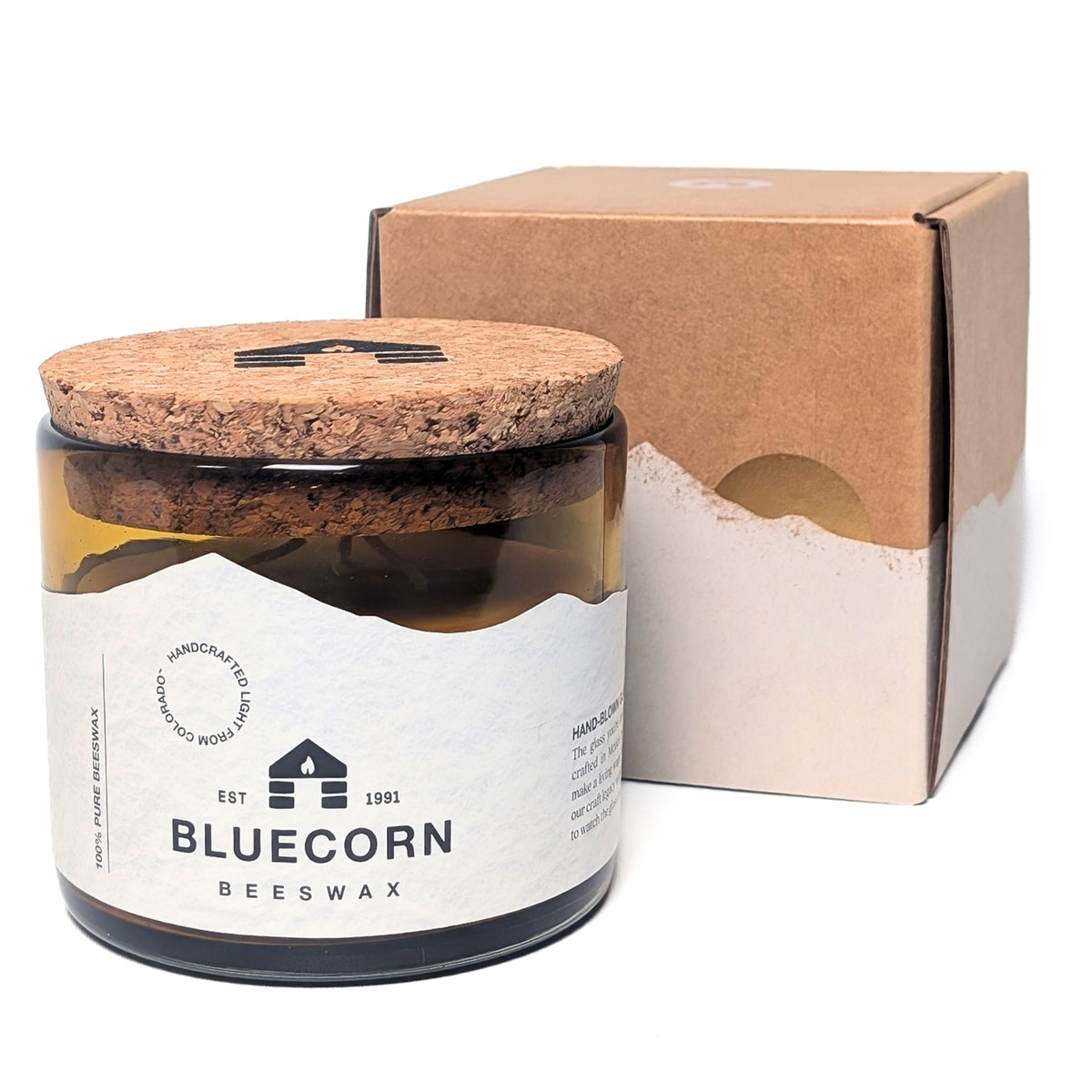 Beeswax jar 22oz 3-Wick candle in a blown glass holder with white bluecorn label and cork lid next to a small charming square kraft gift box with white mountains and a white background