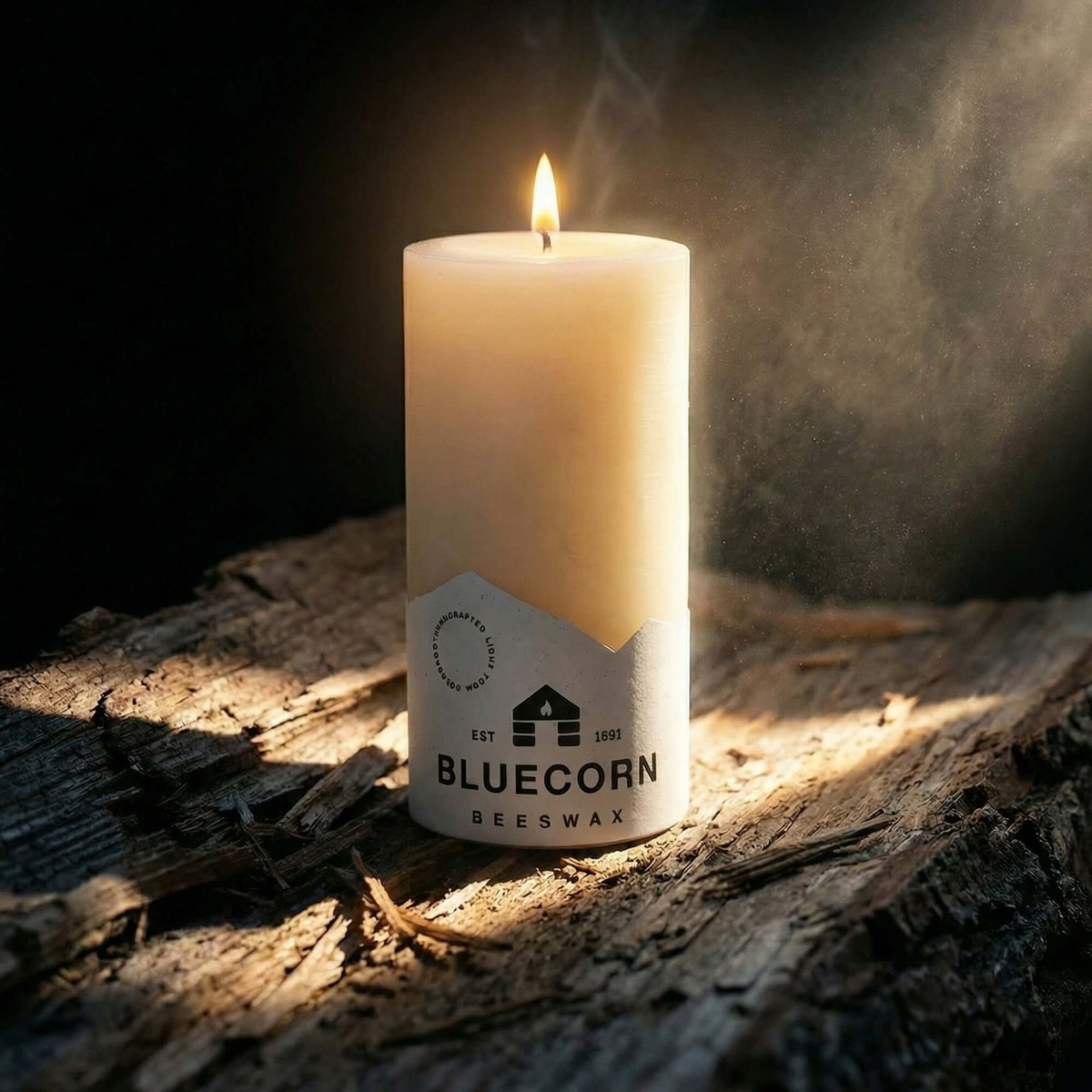 A lit Ivory pure beeswax pillar candle from bluecorn candles with white bluecorn label on a rustic wooden surface