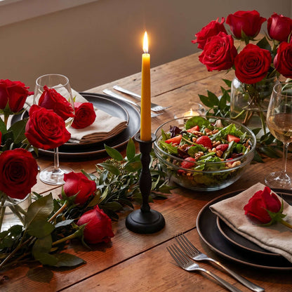 Elegant dining setting featuring hand-dipped beeswax taper candles and fresh red roses.