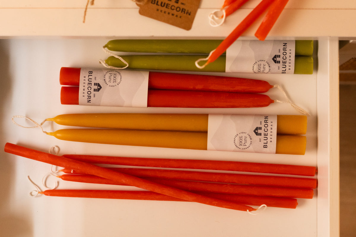 A drawer filled with full sized Apricot, Raw and Pistachio Green taper candles with white bluecorn label next to Apricot thin tapers 