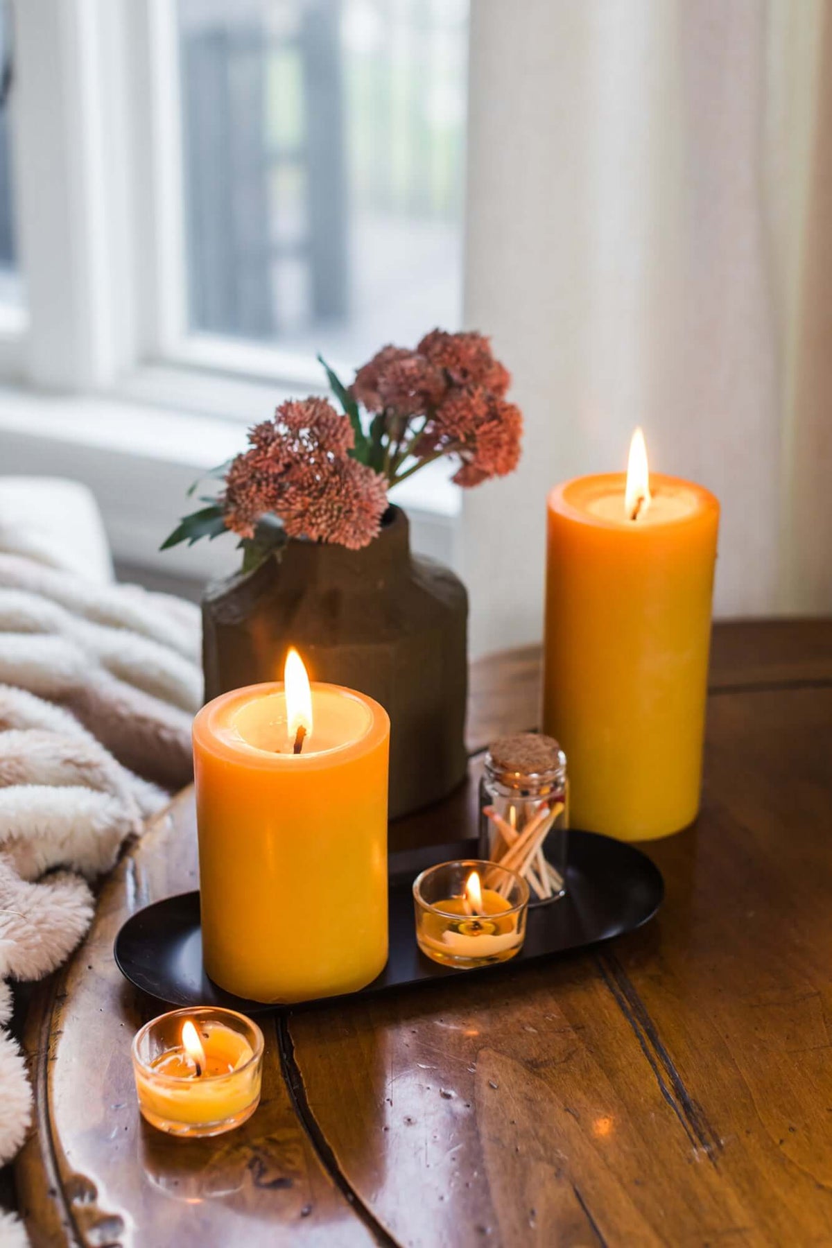 Candlelit scene with three candles on a wooden surface, including a large yellow candle, a small candle, and a decorative vase with flowers.