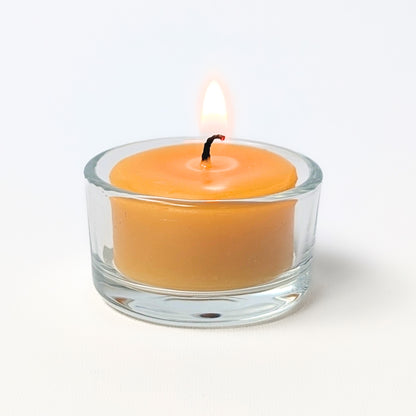 Yellow candle in a clear glass tea light holder on a white background