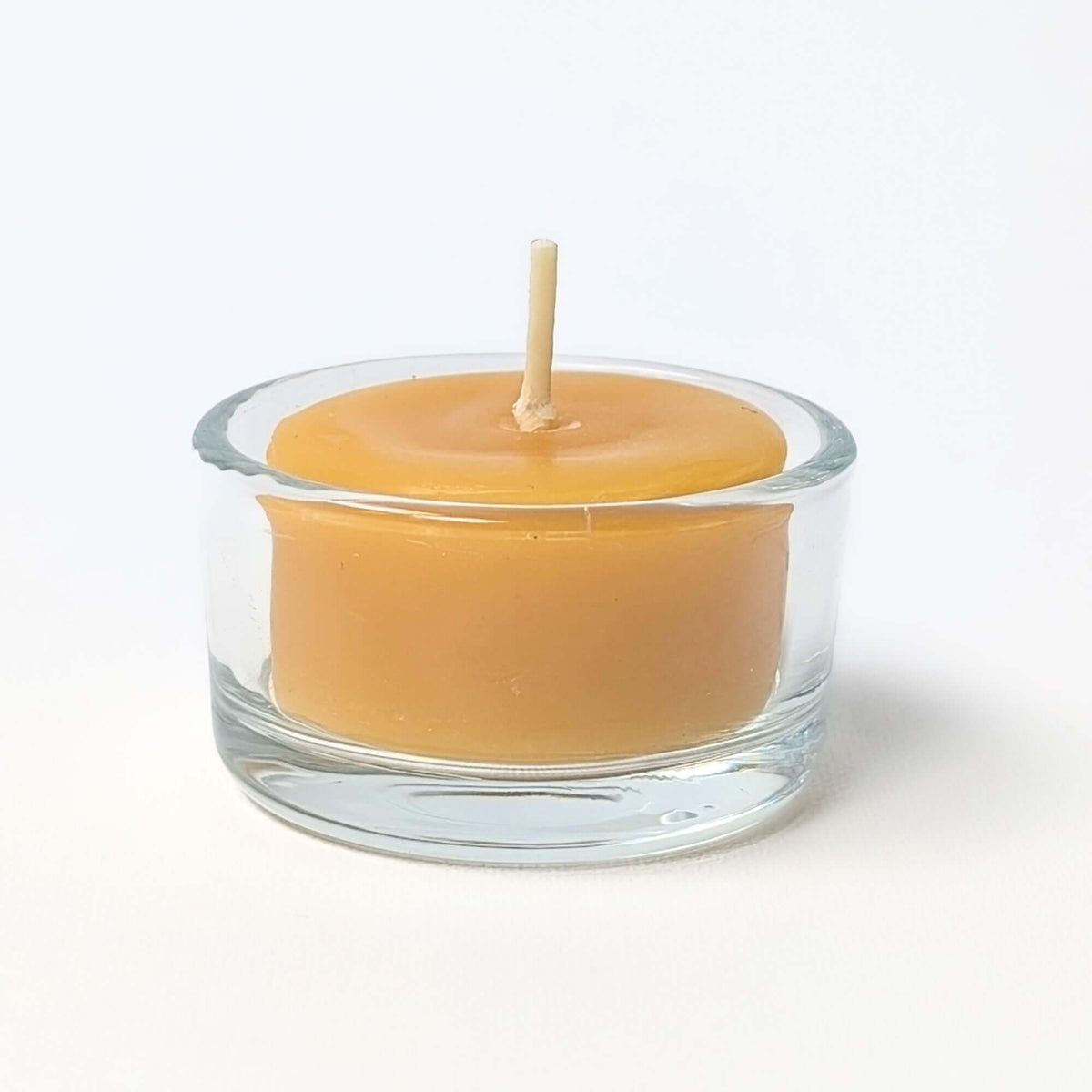 Beeswax candle in a clear glass holder on a white background