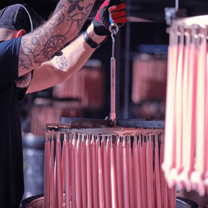 A craftsman dips pink beeswax taper candles made from pure beeswax for Bluecorn Candles