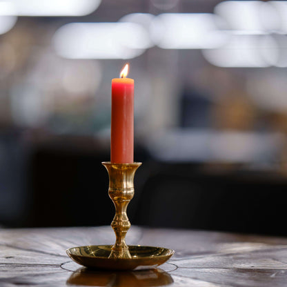 beeswax taper candles - A pink candlestick made of pure beeswax burns in a brass taper candle holder at Bluecorn Candle's workshop in Colorado