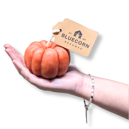 Pumpkin shaped candle being held in a hand, showcasing its orange beeswax design and tag from Bluecorn Beeswax.