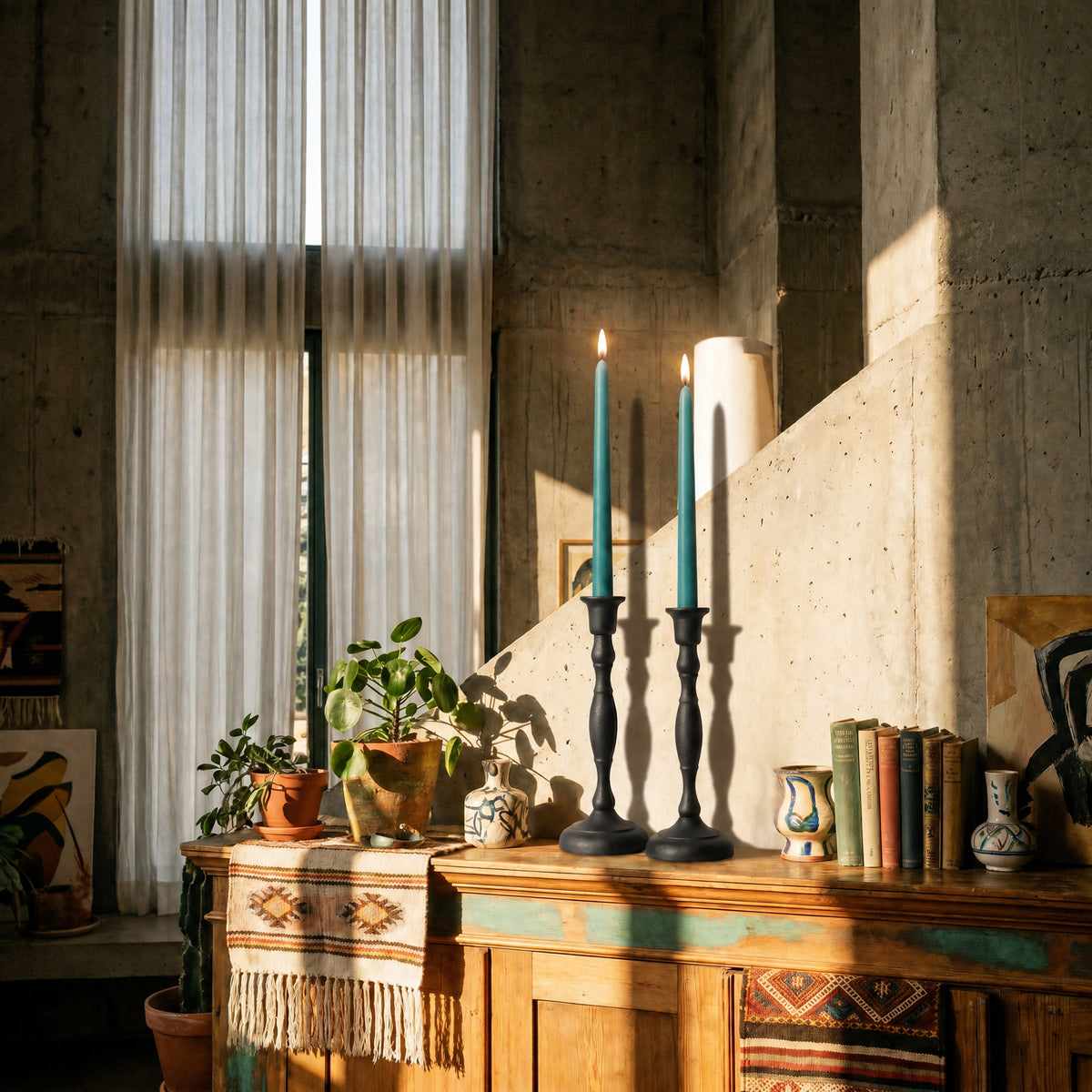 Teal beeswax taper candles placed in elegant candlesticks on a rustic wooden tabletop, surrounded by greenery and decor.