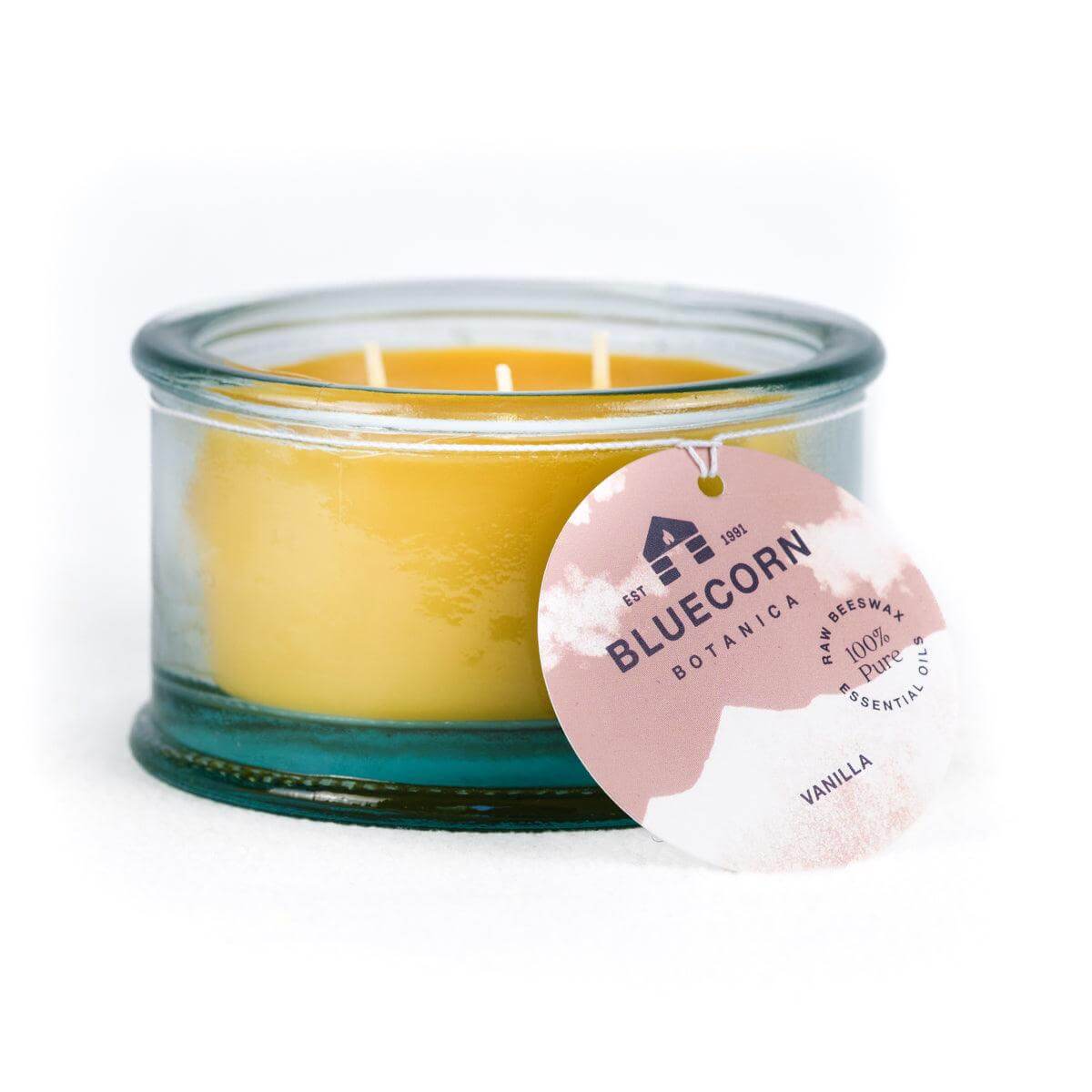Bluecorn Botanica 100% Pure Beeswax scented candle - Vanilla 10oz 3-Wick Glass Candle. Wax is golden in color and glass is clear colored, with a white back drop. Features light brown Bluecorn Botanica hang tag printed on 100% recycled paper with Bluecorn name and logo. Burn Time: 18 hours. Made with 100% Pure Beeswax, 100% Pure Essentail Oils and a 100% pure cotton wick, no lead. Candles are paraffin free, clean burning and non-toxic.